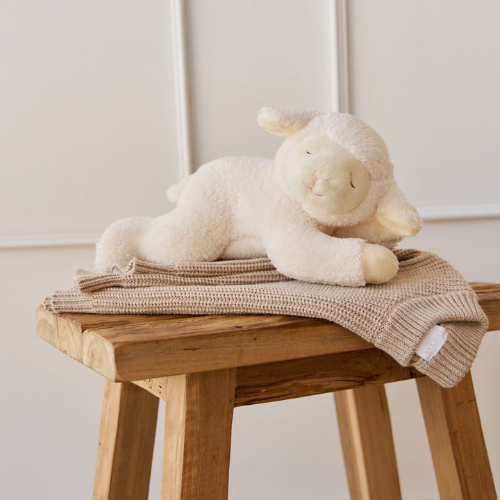White plush lamb toy on a wooden stool with a beige blanket